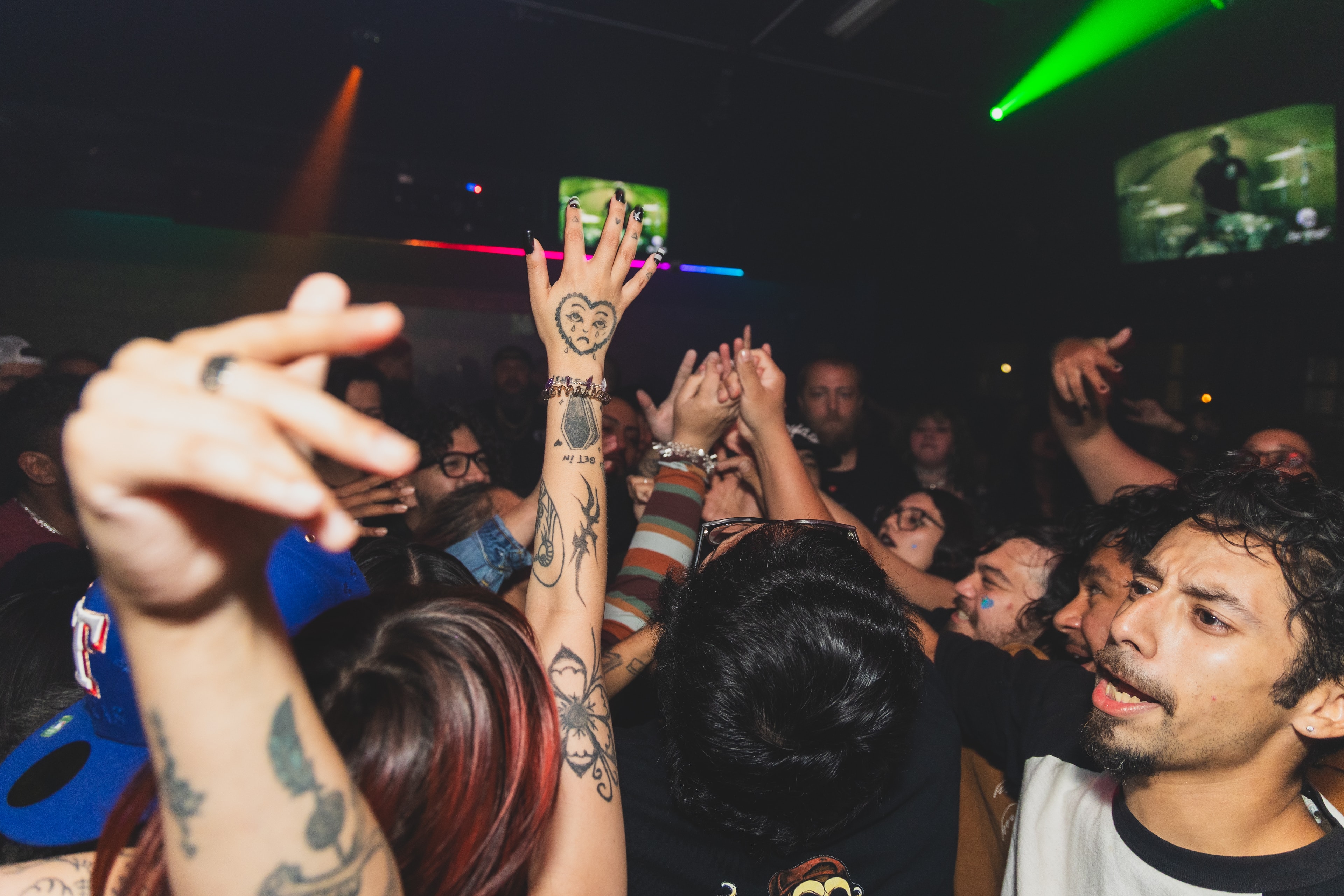 Crowd with hands raised under laser lights at SATX Emo Club