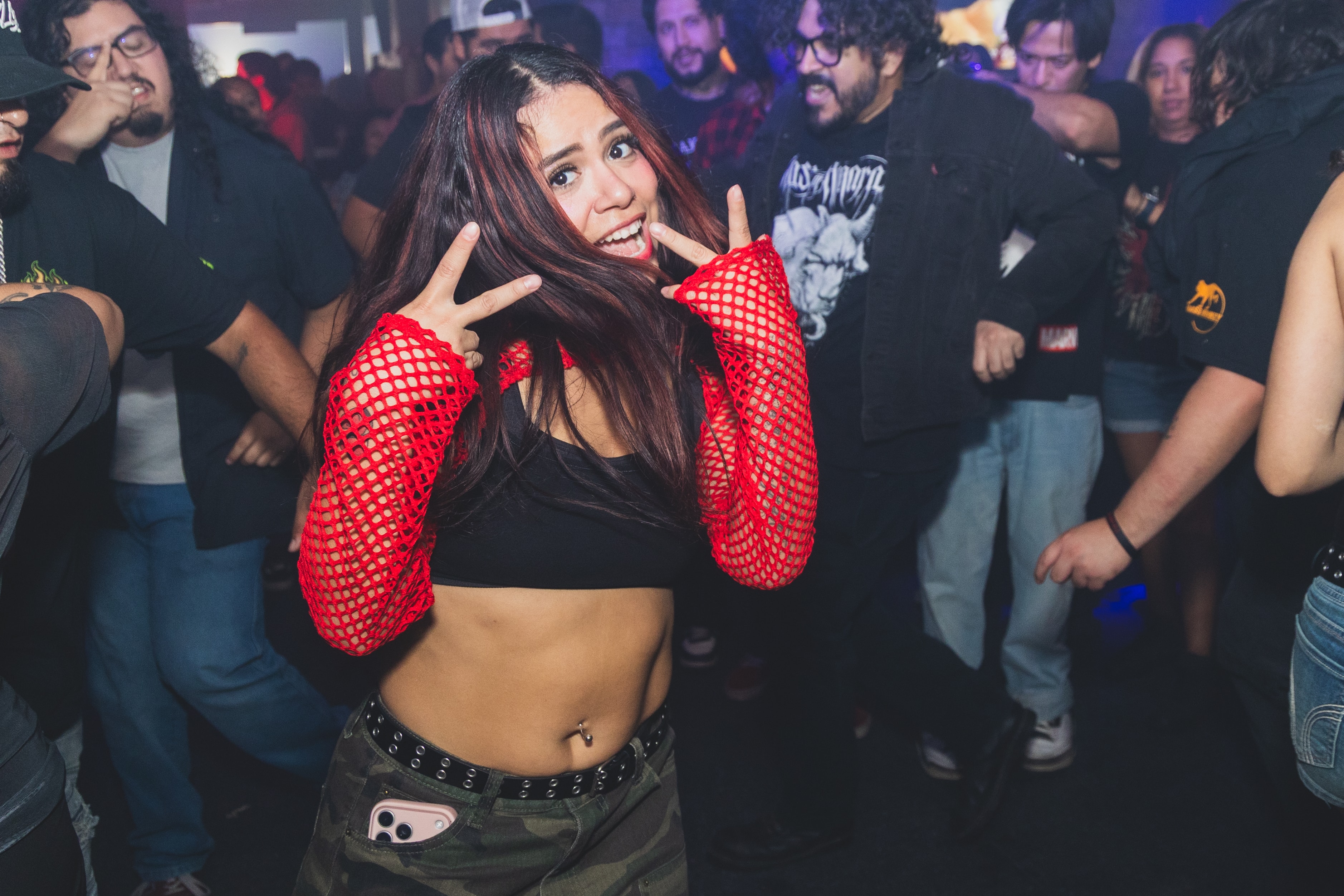 Woman in red fishnet sleeves throwing peace signs on the dance floor at SATX Emo Club