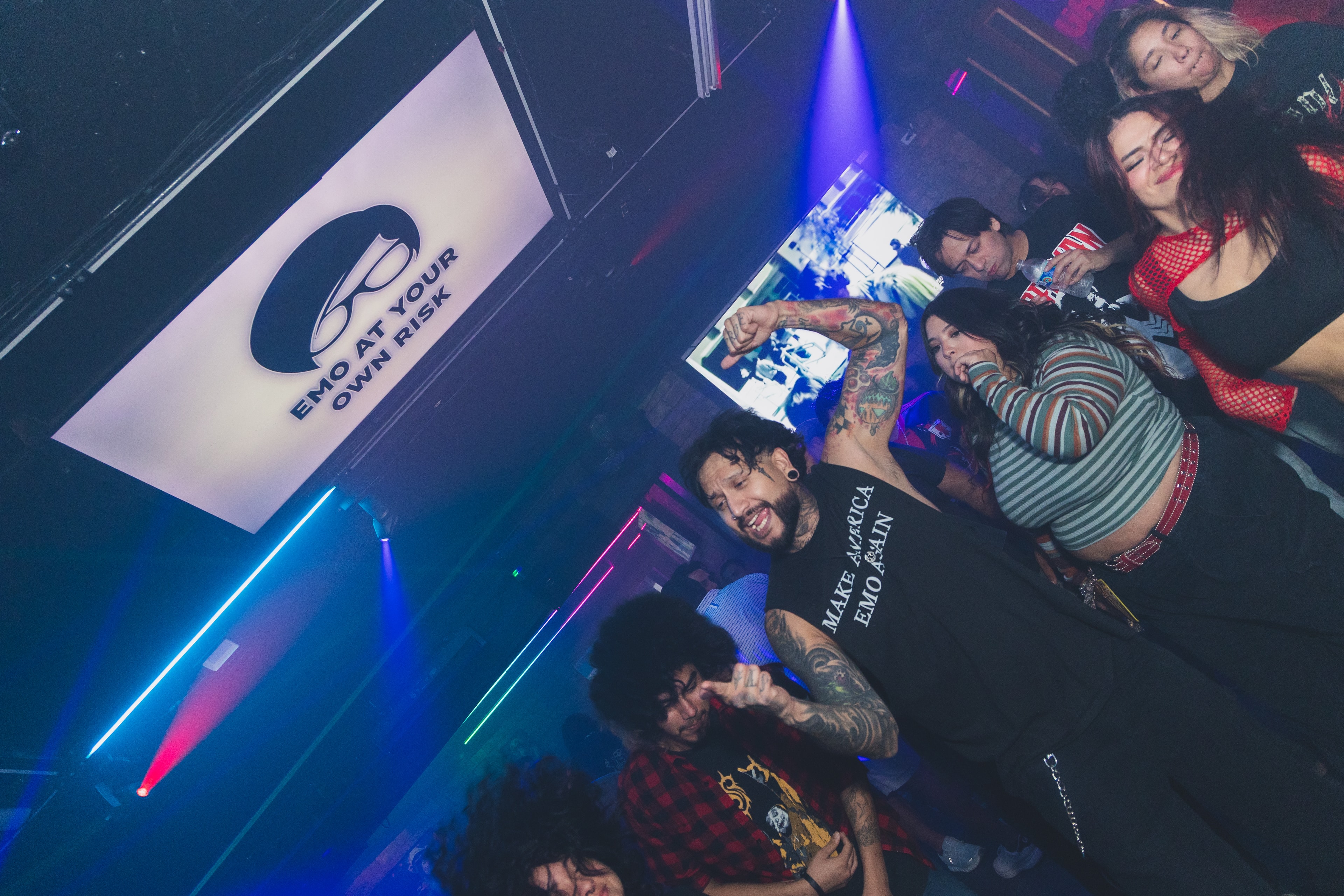Group posing under the Emo At Your Own Risk screen at SATX Emo Club