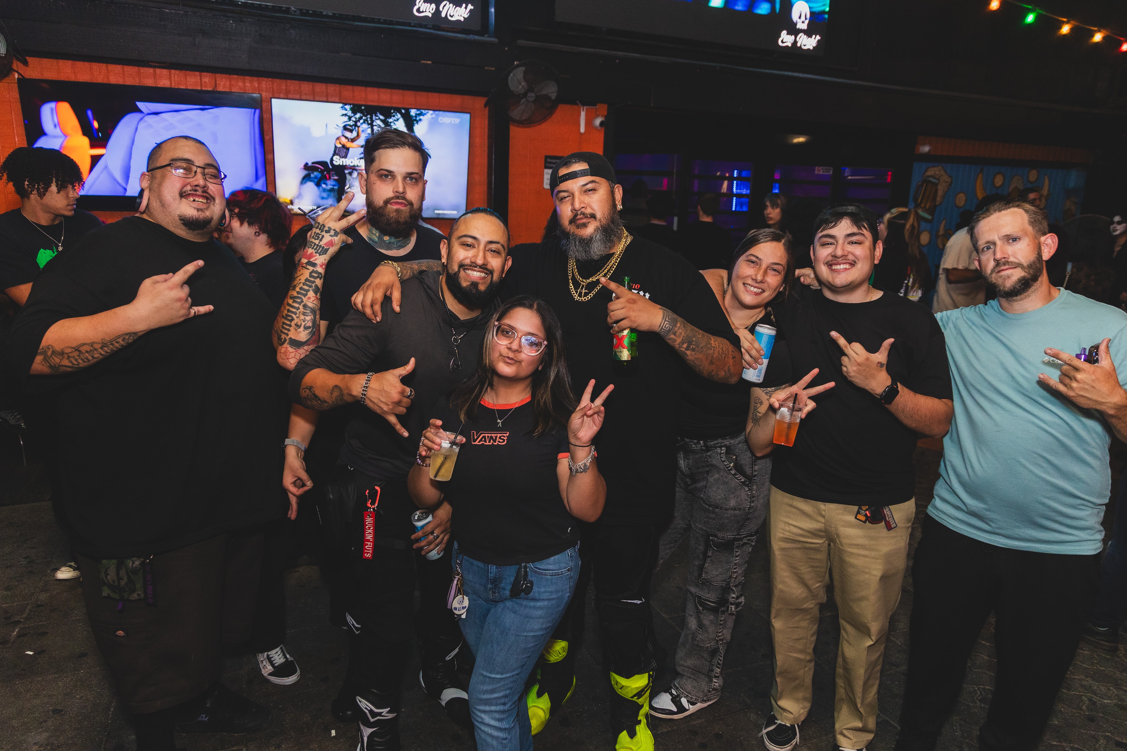 Large group of friends throwing horns and peace signs under Emo Night signs at SATX Emo Club