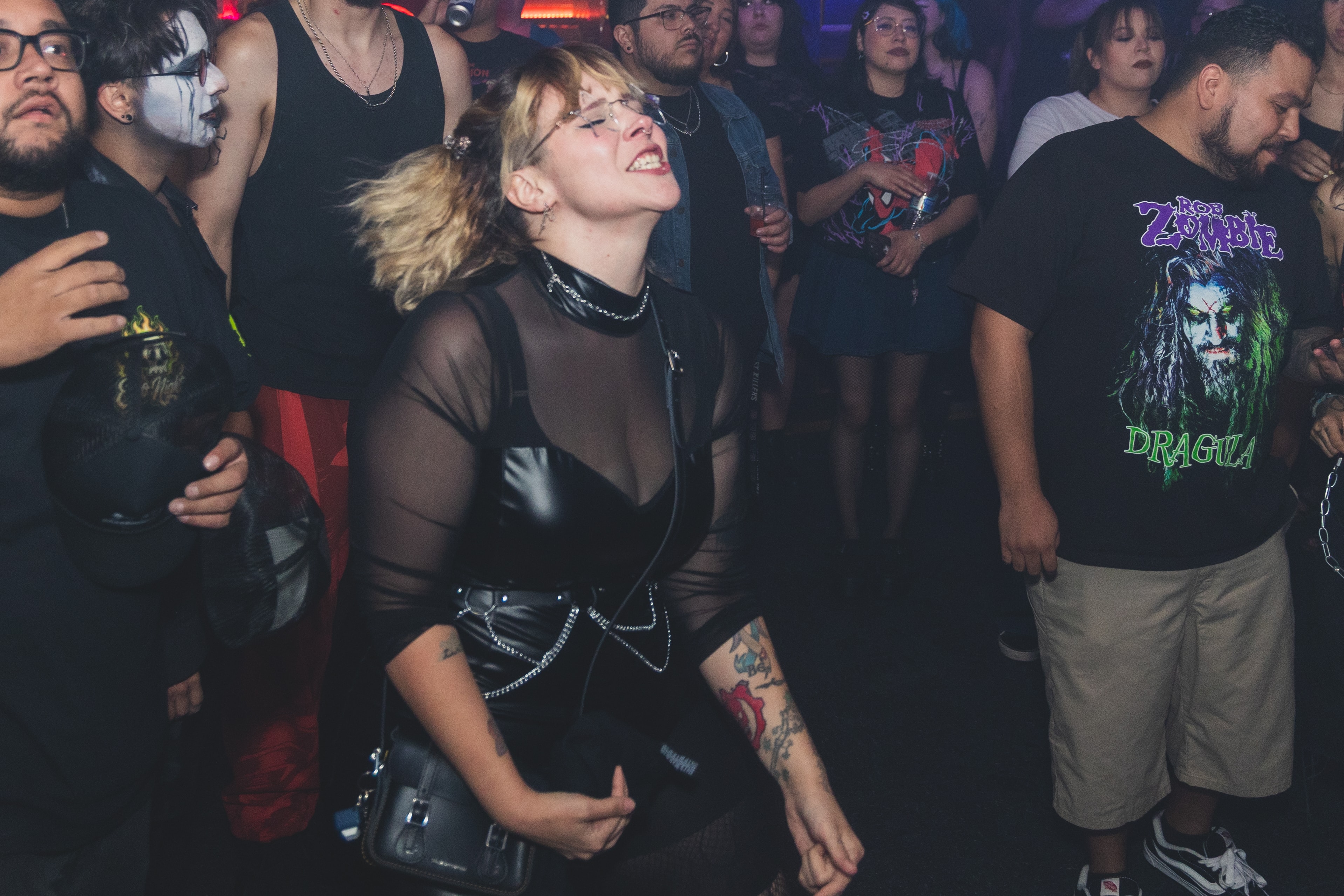 Woman in mesh top and chains dancing with eyes closed next to Rob Zombie Dragula tee at SATX Emo Club